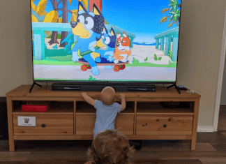 A baby and a young child watching Bluey on a TV at home.