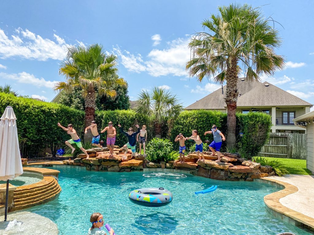 8 Kids jumping into a backyard pool. 