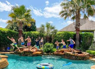 A photograph of 8 kids jumping into a backyard pool.