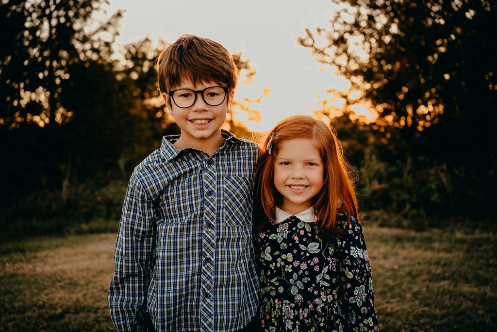A boy wearing a plaid button down and a girl wearing a floral dress pose for family photos.