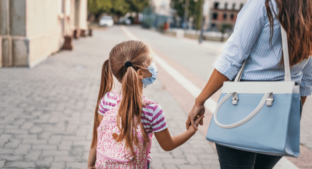 working mom holding daughters hand as they walk to school