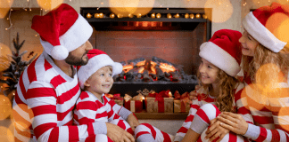 family in matching holiday pajamas sits by fire