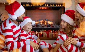 family in matching holiday pajamas sits by fire