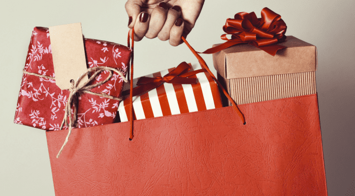 woman's hand holding a holiday shopping bag filled with wrapped gifts