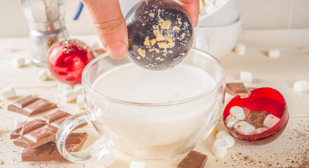 hand holding hot chocolate bomb over a cup of milk