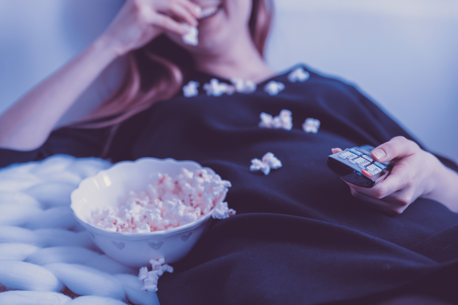 woman spills popcorn on herself while holding TV remote
