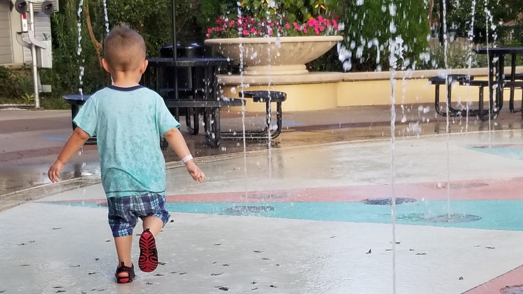 preschooler with back turned walks through splash fountains