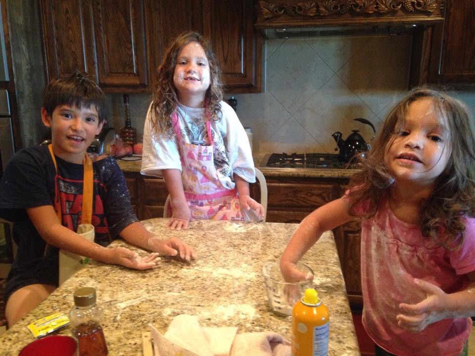 Three children with aprons bake on kitchen island