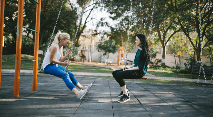 mom friends sit opposite each other on playground swings