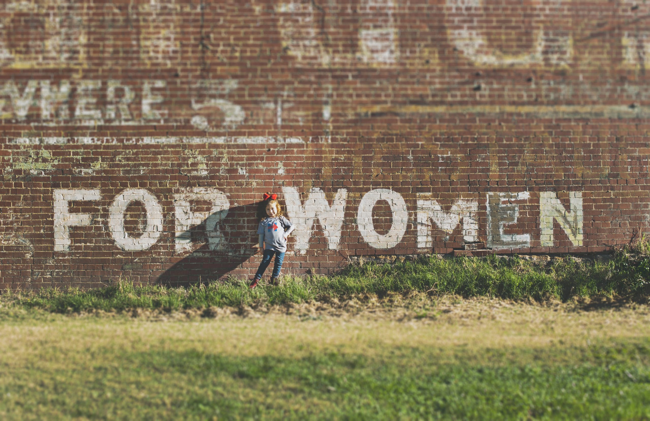 little girl stands in front of a brick wall that says "For Women"
