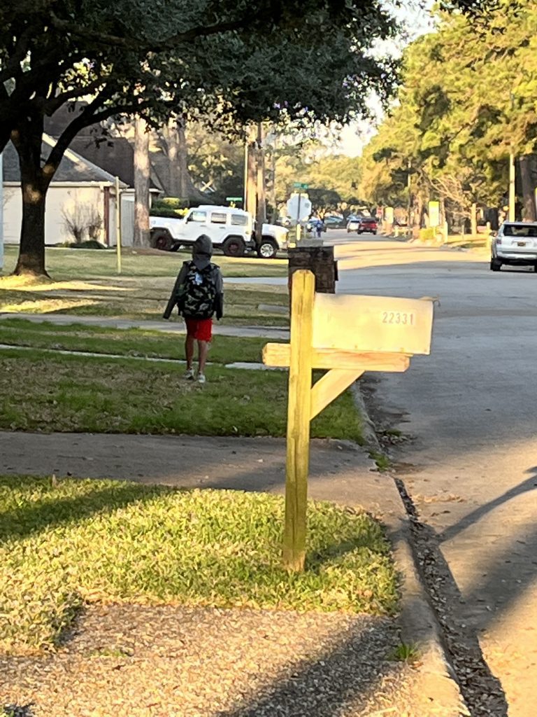 boy with backpack walks down a neighborhood street