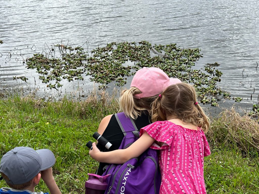 small child embraces mother while they look at the edge of a lake