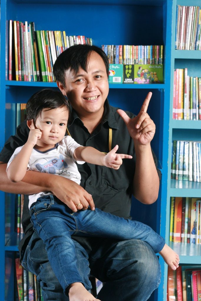 father and toddler son sit in chair at library