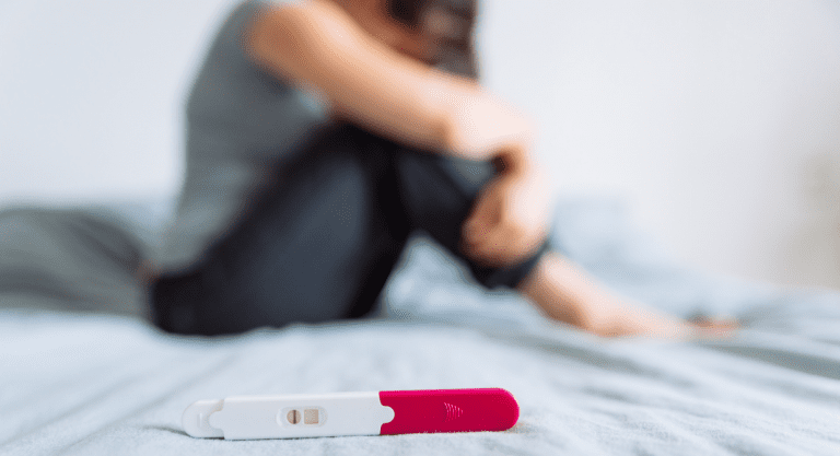 woman sits on bed in front of negative pregnancy test