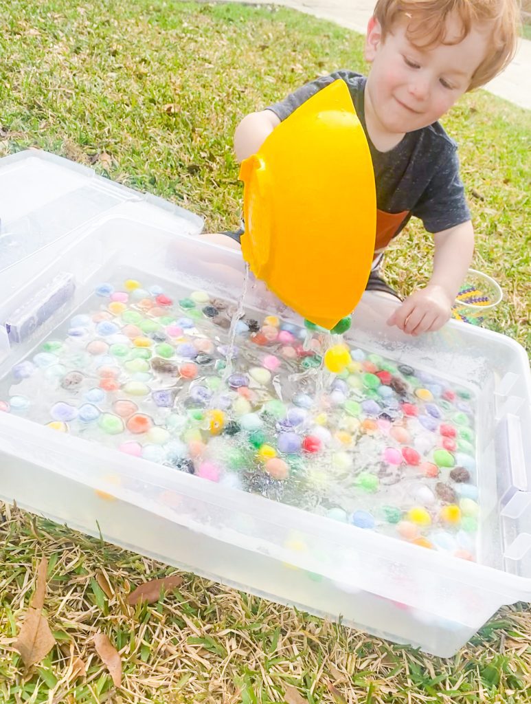 child plays with pom pom balls in a plastic container filled with water 