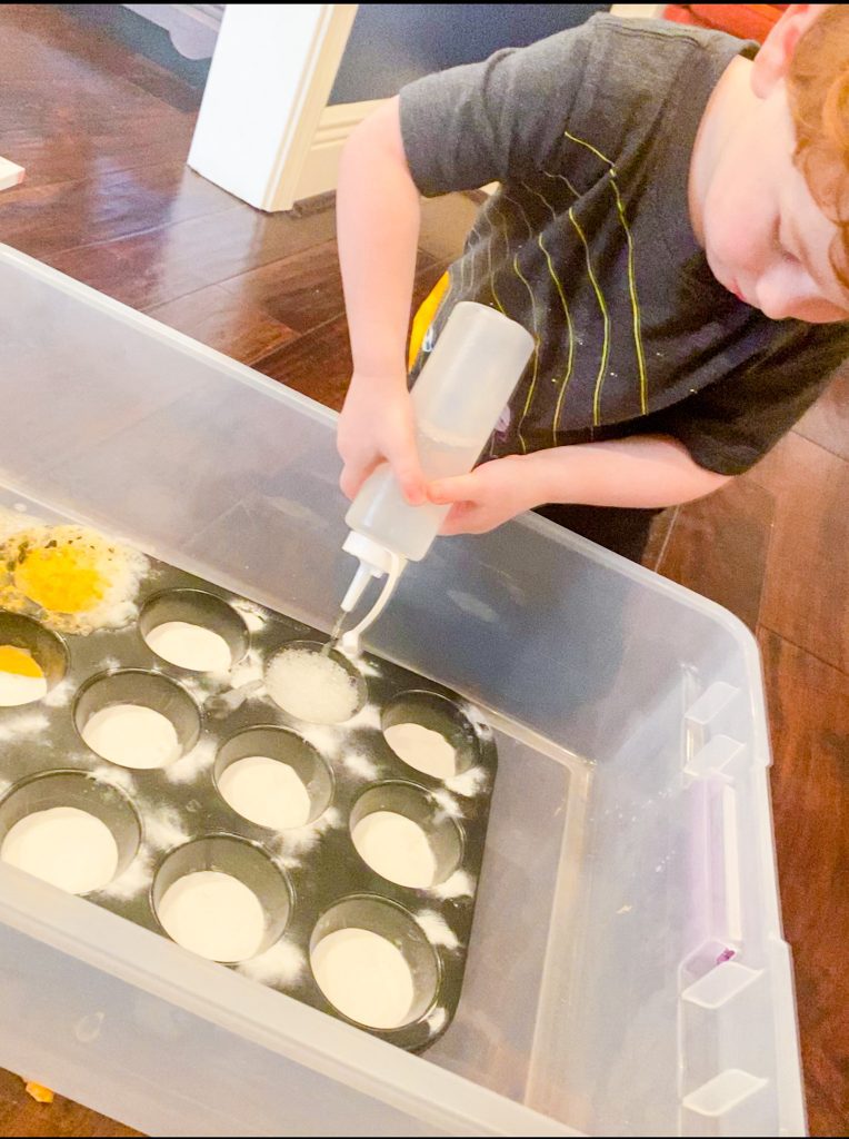 child squirts vinegar into muffin tins filled with baking soda
