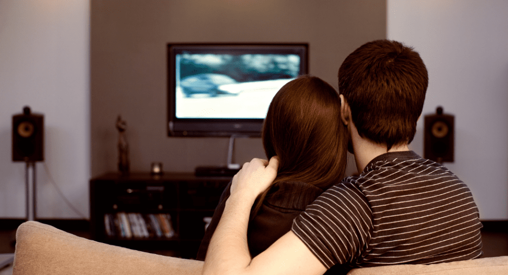 couple sits on couch watching tv