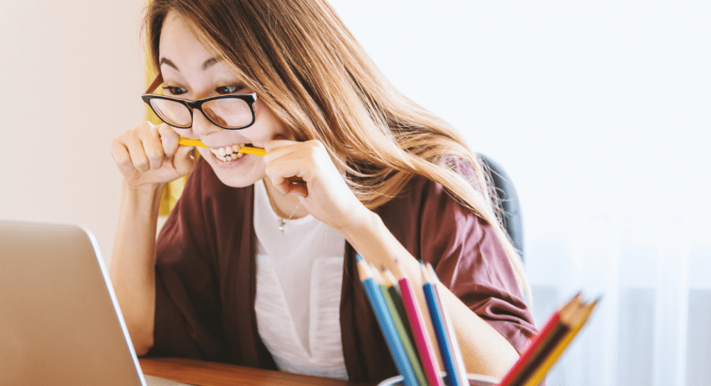 woman chews on pencil while looking at computer