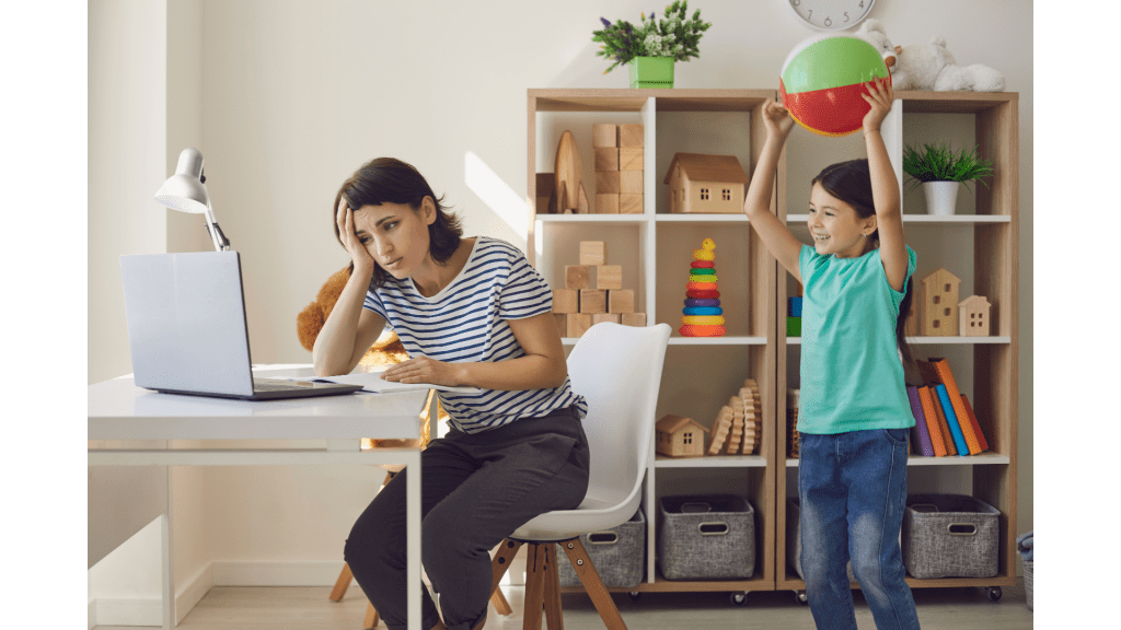 frustrated mother looks at laptop while her son stands behind her holding a beach ball