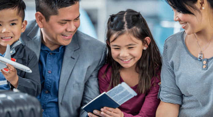 3 Reasons to Travel with Your Children family smiles as they look at plane tickets