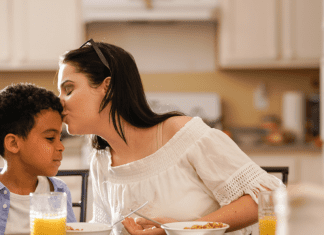 mother kisses son on his head at the breakfast table
