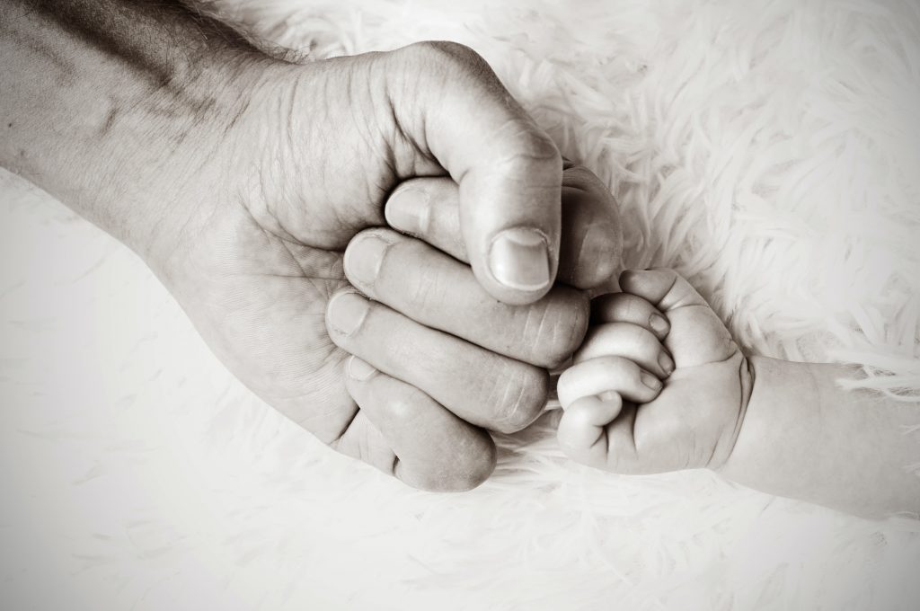 man's hand holding infant hand