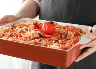 woman's hands hold a casserole dish of spaghetti