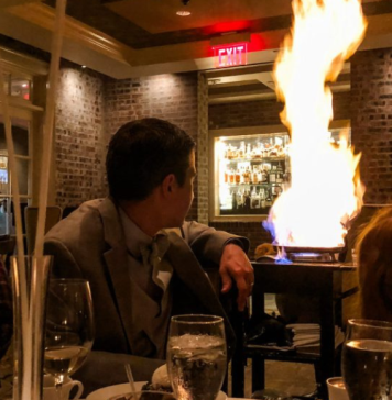 family sits at restaurant table looking at flame behind them