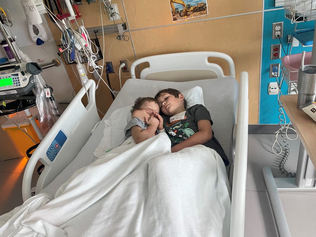 two young children cuddle in hospital bed