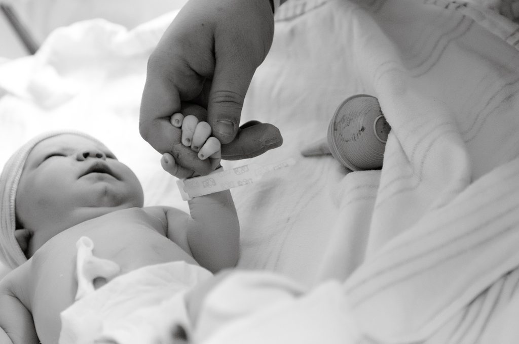 newborn baby holding adult finger