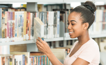 young girl stands at library shelf and selects a book
