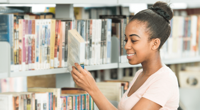young girl stands at library shelf and selects a book