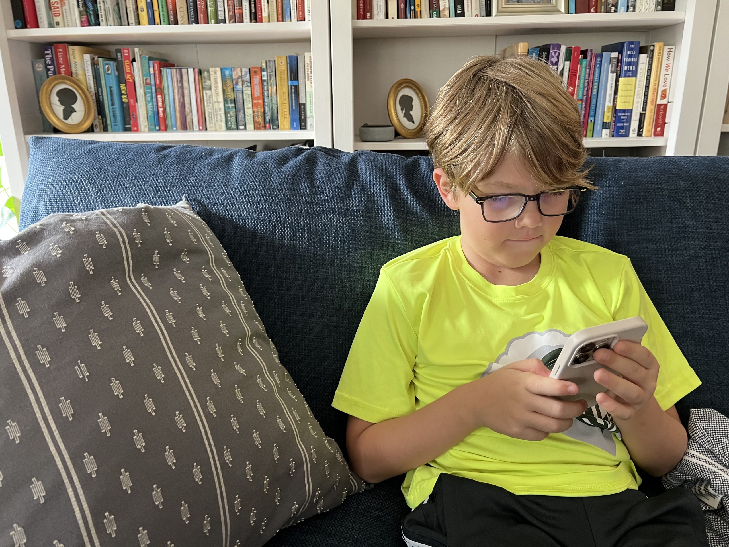 young boy sits on couch looking at phone