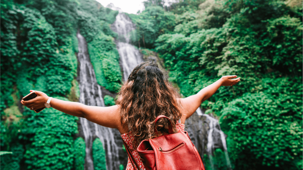 woman with arms outstreatched stands in front of waterfall