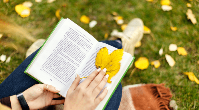 woman sits in grass reading using leaf as bookmark