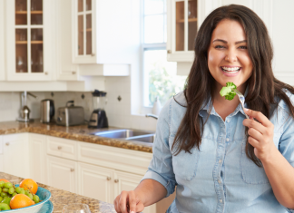 woman smiling while eating a bite of broccoli