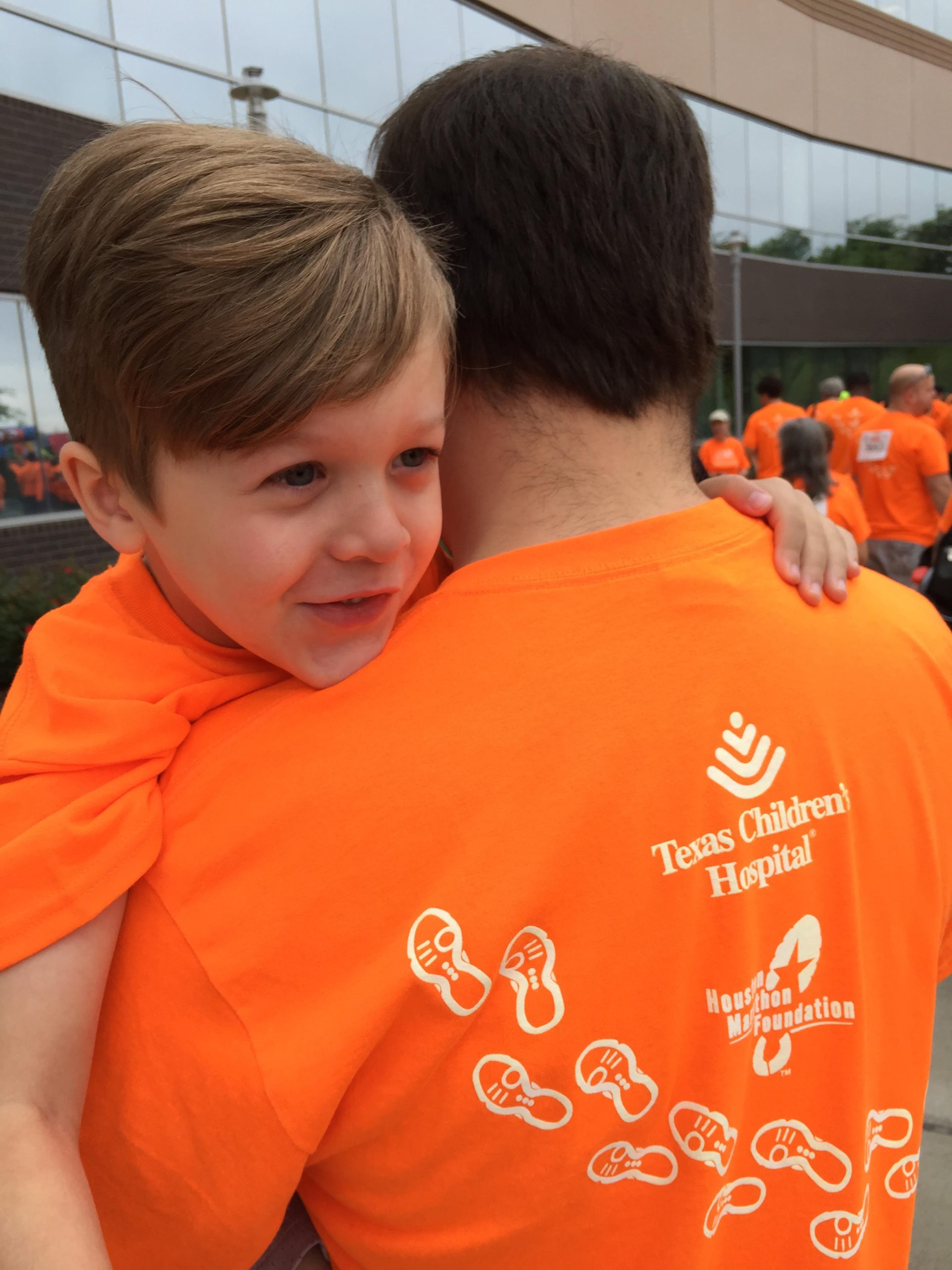 father and young son embrace, wearing matching orange t shirts