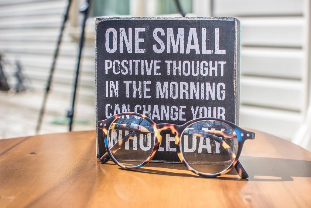 glasses in front of wooden block with positive affirmation written on it