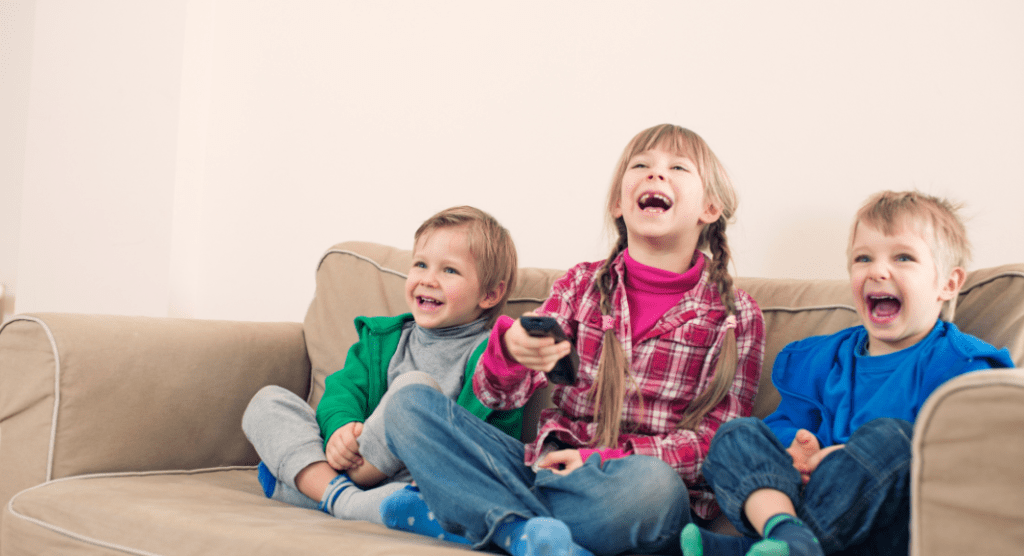 three preschoolers on couch with remote, laughing