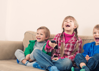 three preschoolers on couch with remote, laughing