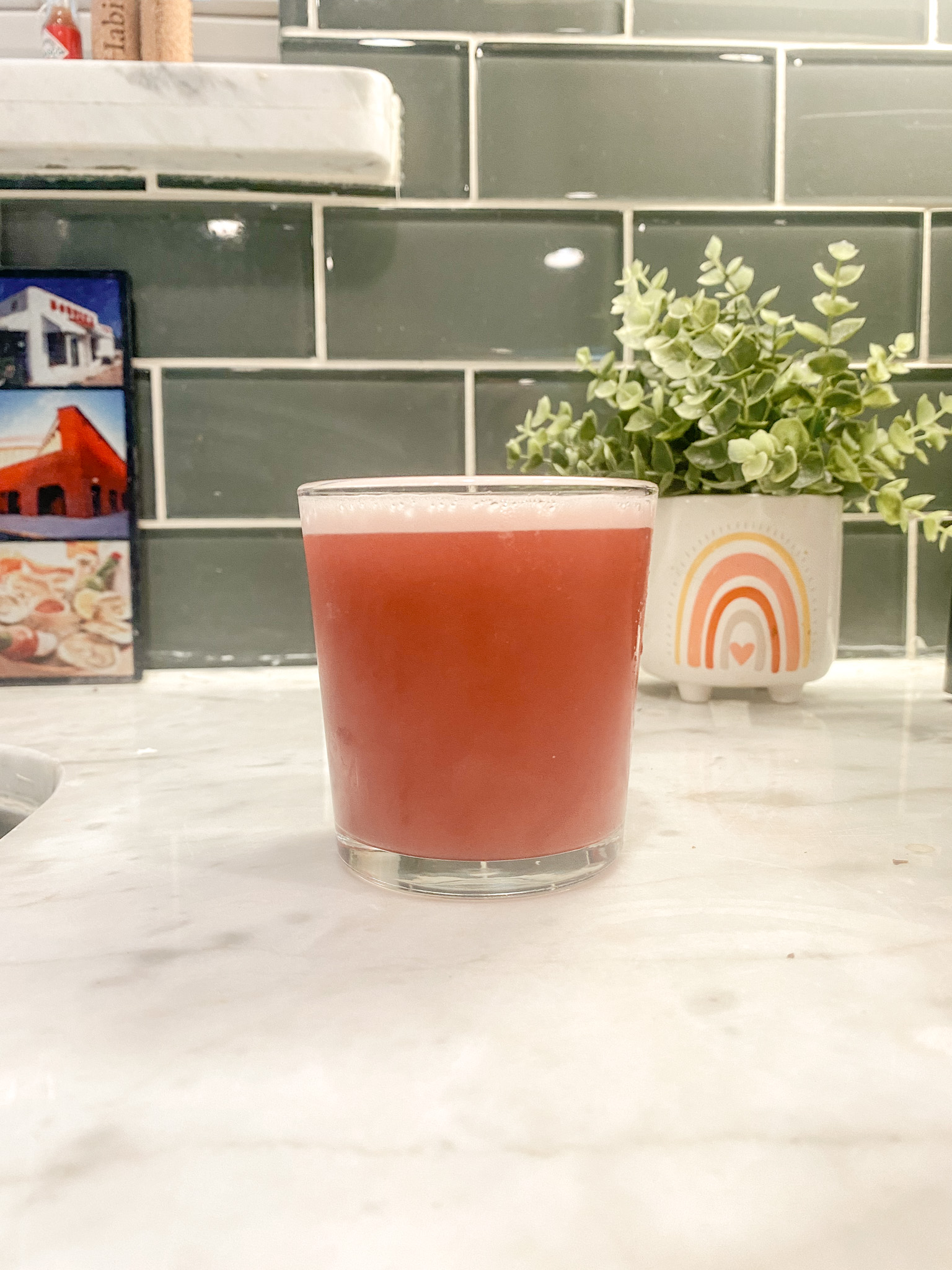 Pink cocktail sits on counter in front of plant