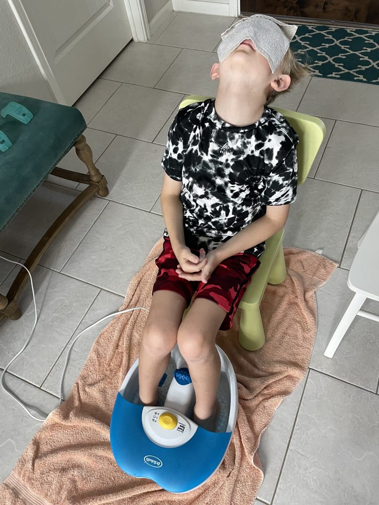 child with feet in foot spa with cloth covering his face