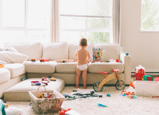 child stands in living room scattered with toys