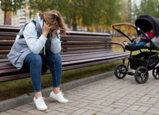 woman sits on bench with head in hands, several feet from a stroller