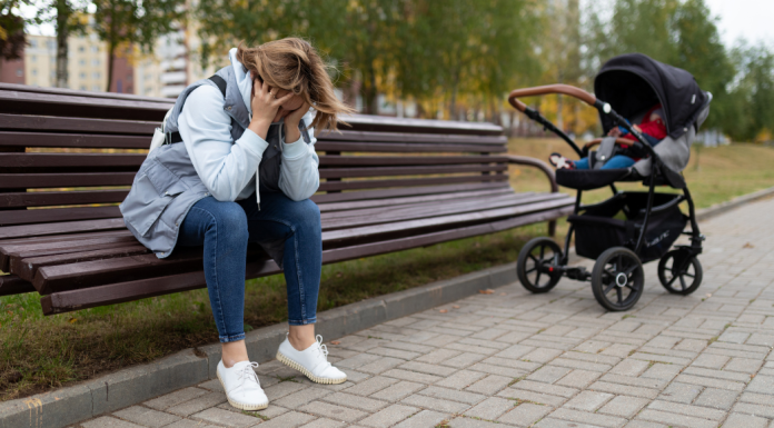 woman sits on bench with head in hands, several feet from a stroller