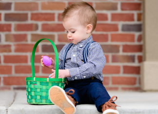 toddler holding pink egg over a green Easter basket