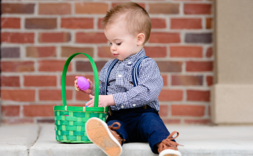 Easter Basket Ideas for Toddlers toddler holding pink egg over a green Easter basket