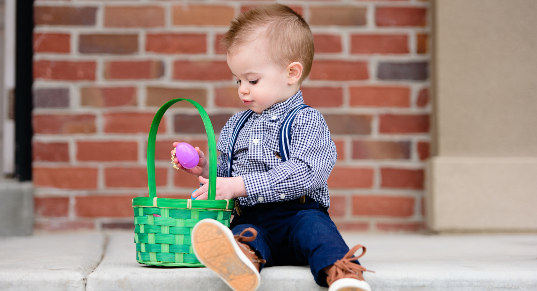 toddler holding pink egg over a green Easter basket