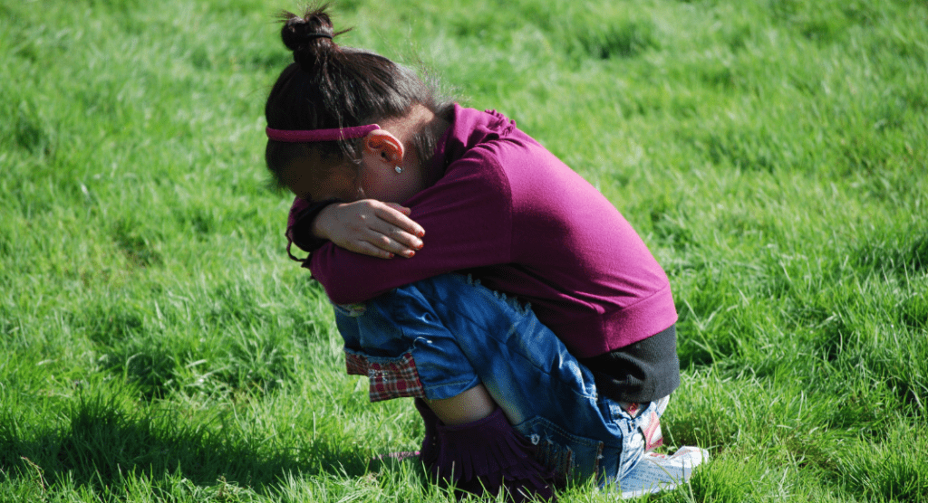 girl crouches in grass, crying