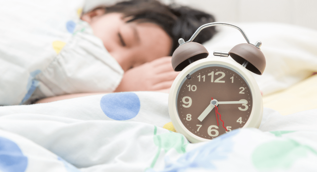 girl in bed asleep with alarm clock resting on bed